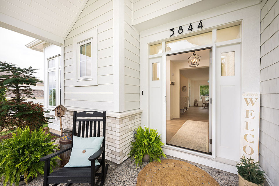 Modern white home entrance with retractable screen door, rocking chair, and potted ferns